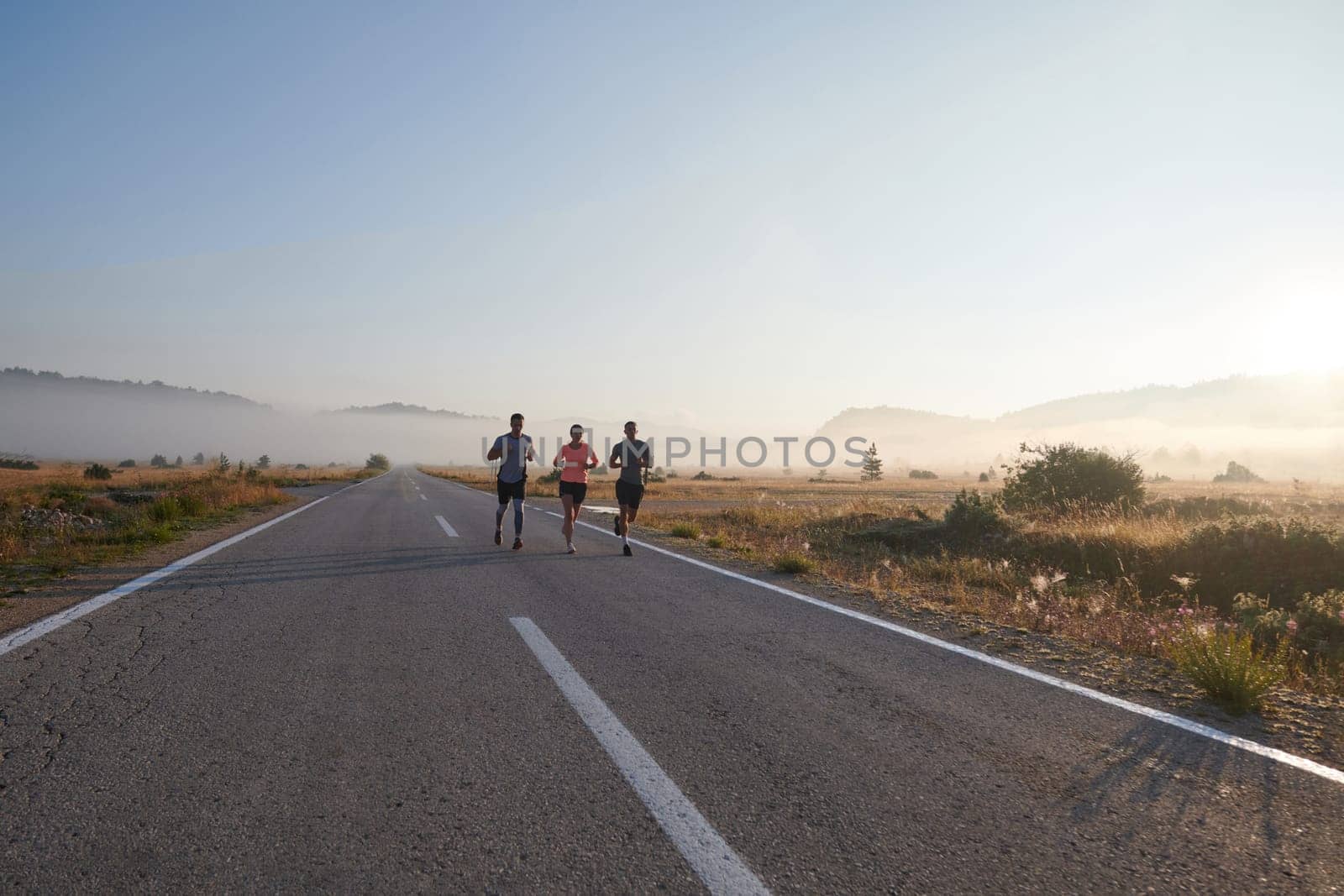 A group of friends, athletes, and joggers embrace the early morning hours as they run through the misty dawn, energized by the rising sun and surrounded by the tranquil beauty of nature.