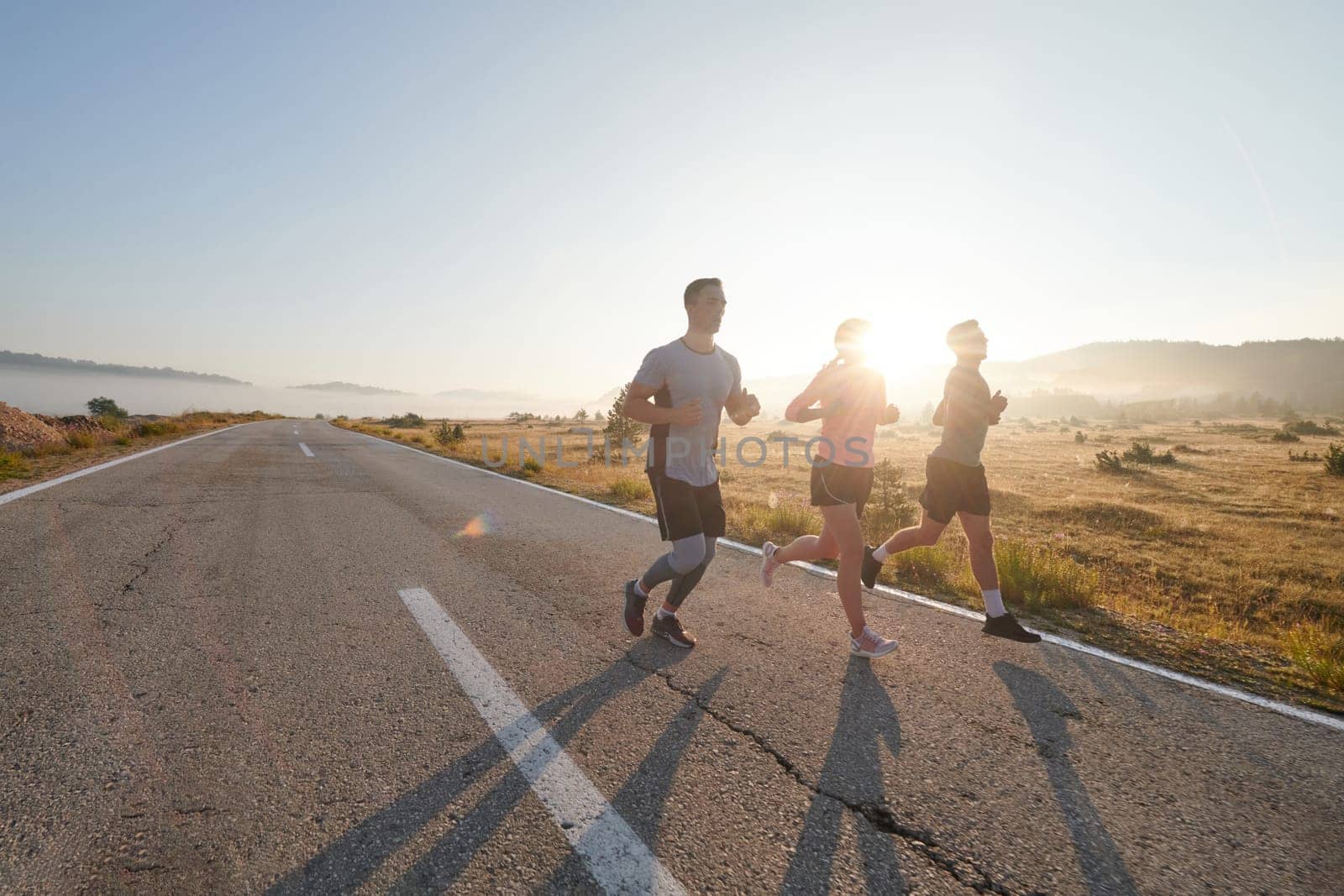 A group of friends, athletes, and joggers embrace the early morning hours as they run through the misty dawn, energized by the rising sun and surrounded by the tranquil beauty of nature by dotshock