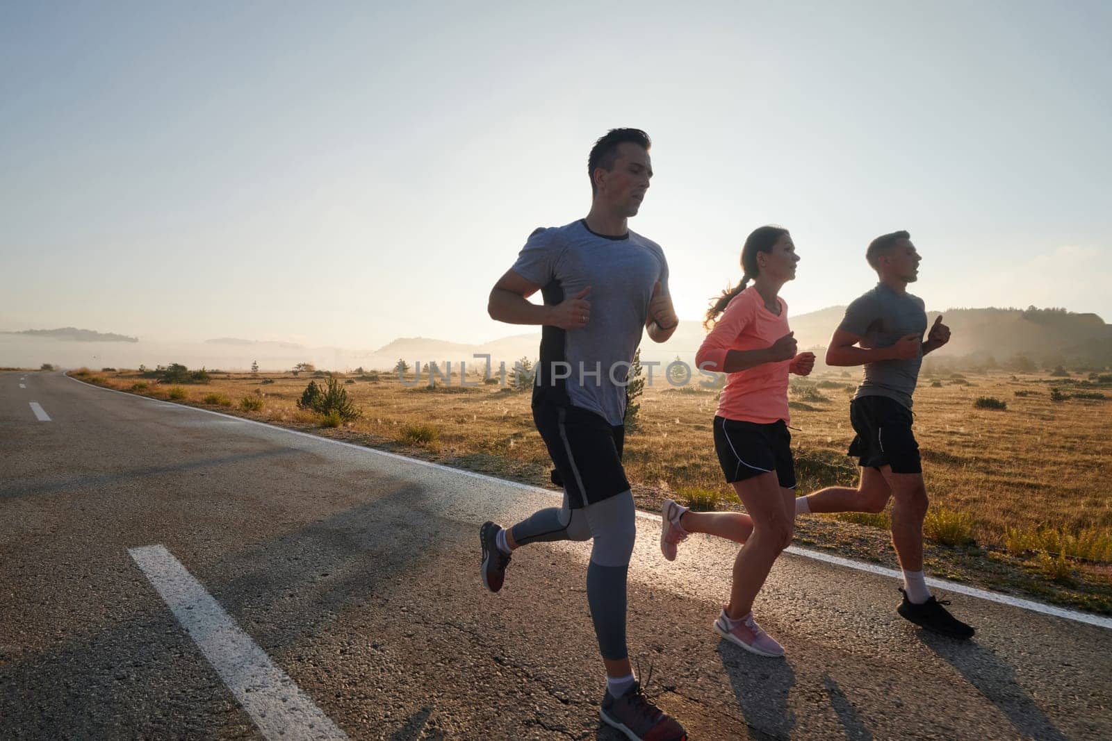 A group of friends, athletes, and joggers embrace the early morning hours as they run through the misty dawn, energized by the rising sun and surrounded by the tranquil beauty of nature.