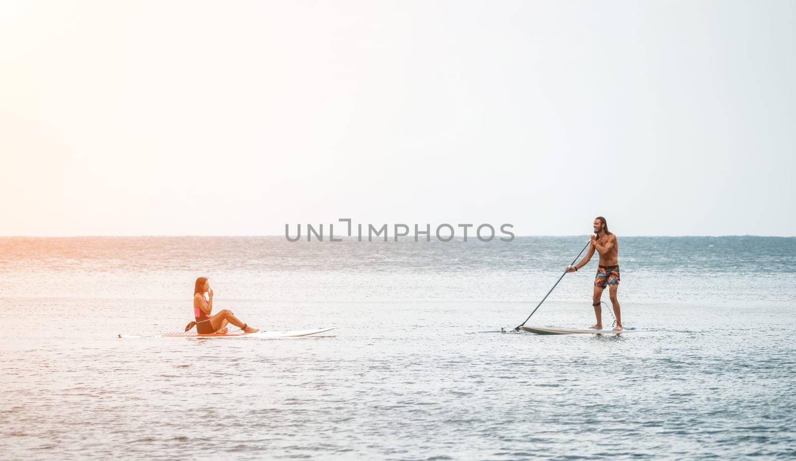 Sea woman and man on sup. Silhouette of happy young woman and man, surfing on SUP board, confident paddling through water surface. Idyllic sunset. Active lifestyle at sea or river