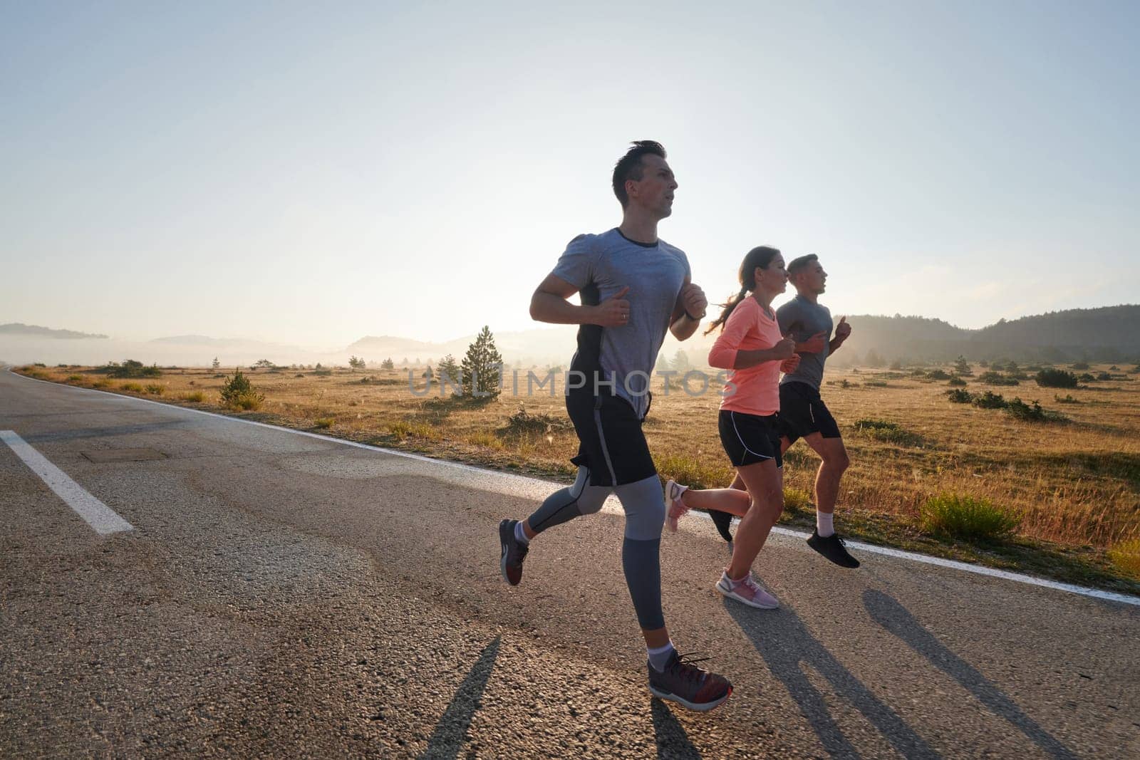 A group of friends, athletes, and joggers embrace the early morning hours as they run through the misty dawn, energized by the rising sun and surrounded by the tranquil beauty of nature by dotshock