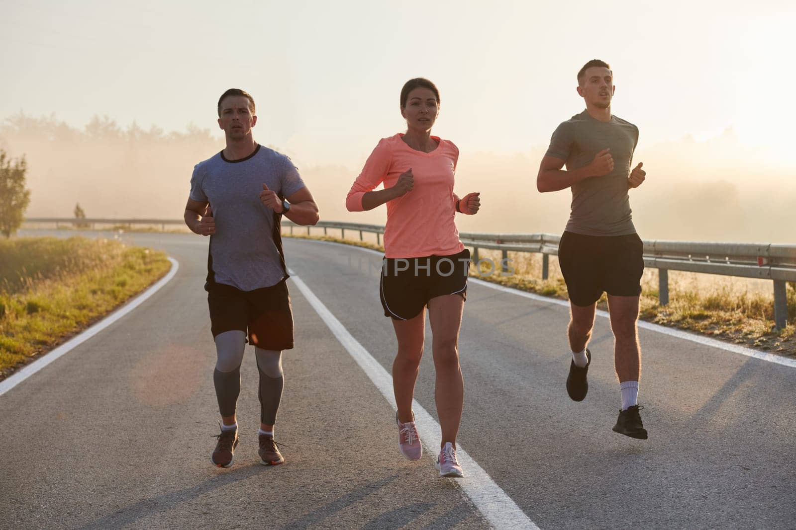 A group of friends, athletes, and joggers embrace the early morning hours as they run through the misty dawn, energized by the rising sun and surrounded by the tranquil beauty of nature.