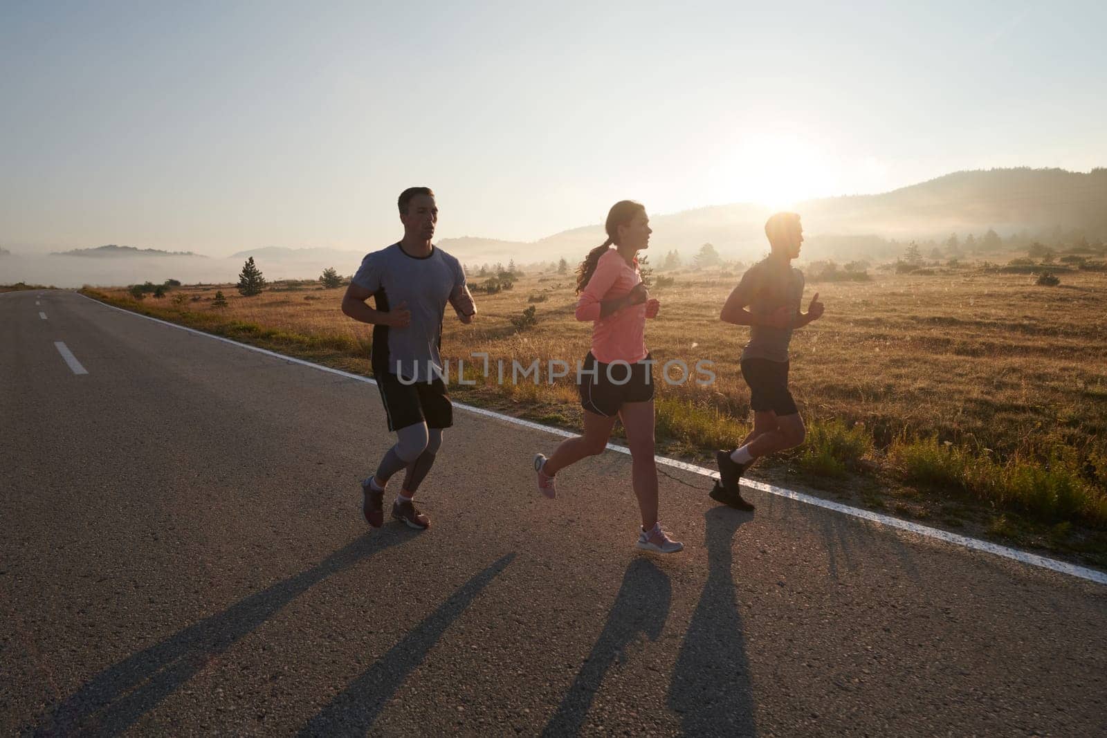 A group of friends, athletes, and joggers embrace the early morning hours as they run through the misty dawn, energized by the rising sun and surrounded by the tranquil beauty of nature.