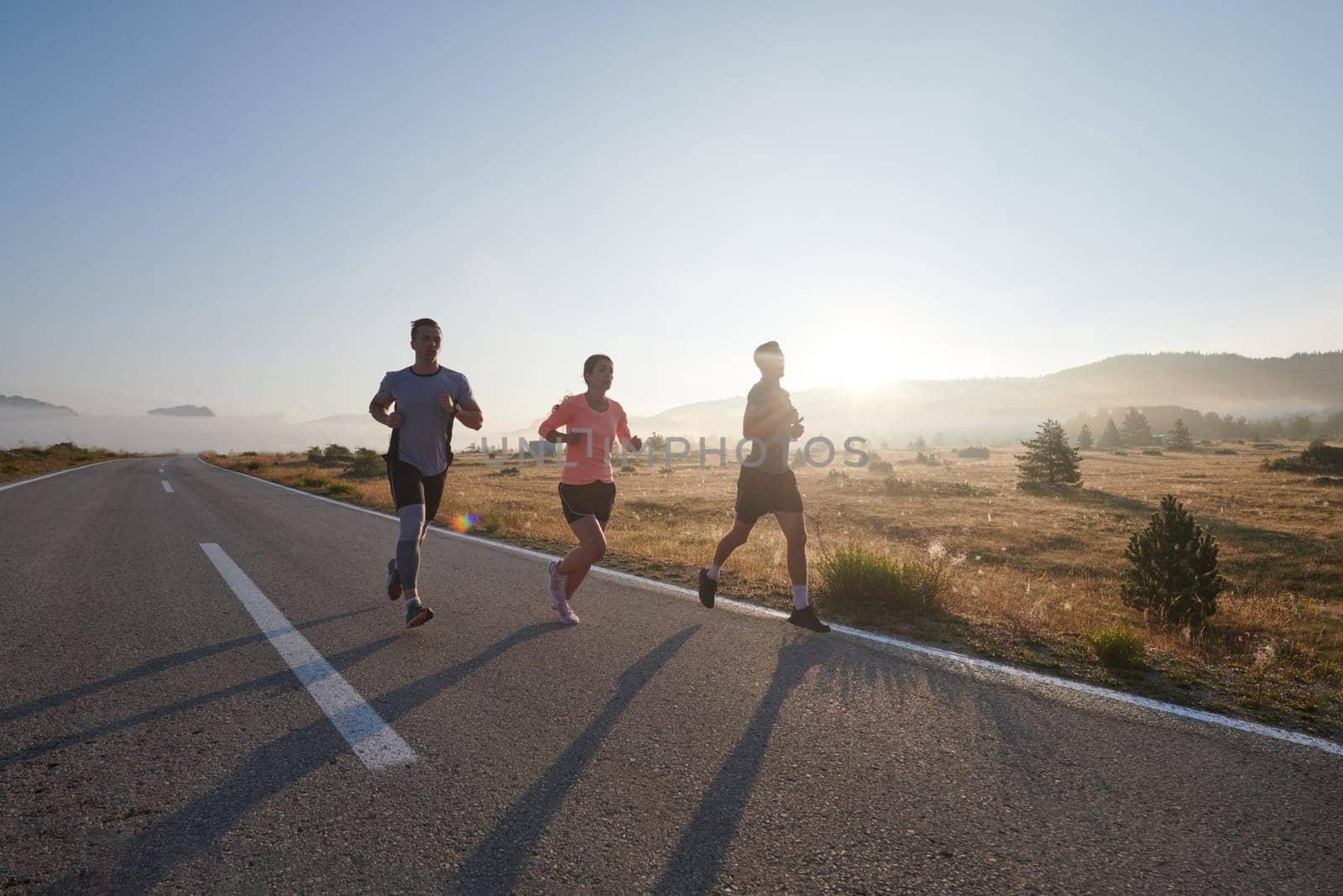 A group of friends, athletes, and joggers embrace the early morning hours as they run through the misty dawn, energized by the rising sun and surrounded by the tranquil beauty of nature by dotshock