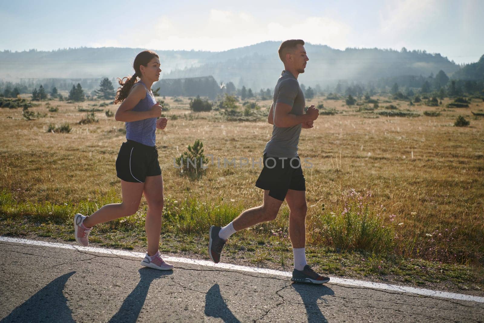 A couple runs through a sun-dappled road, their bodies strong and healthy, their love for each other and the outdoors evident in every stride.