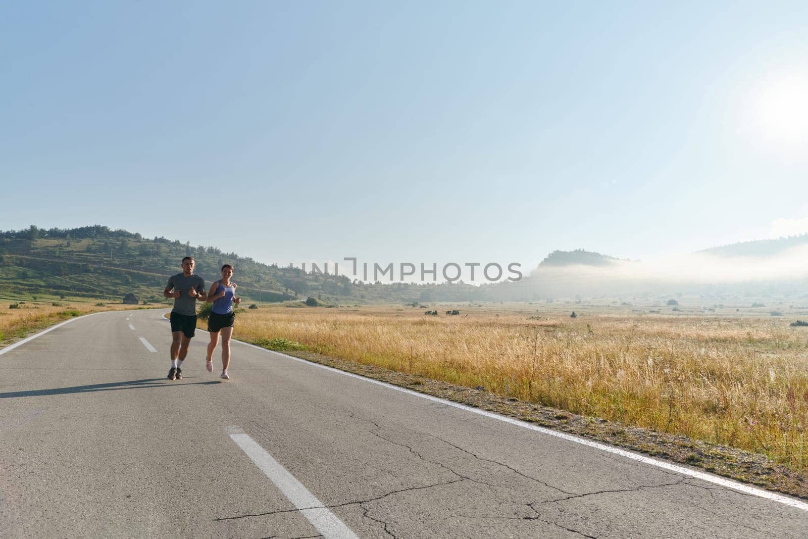 A couple runs through a sun-dappled road, their bodies strong and healthy, their love for each other and the outdoors evident in every stride.