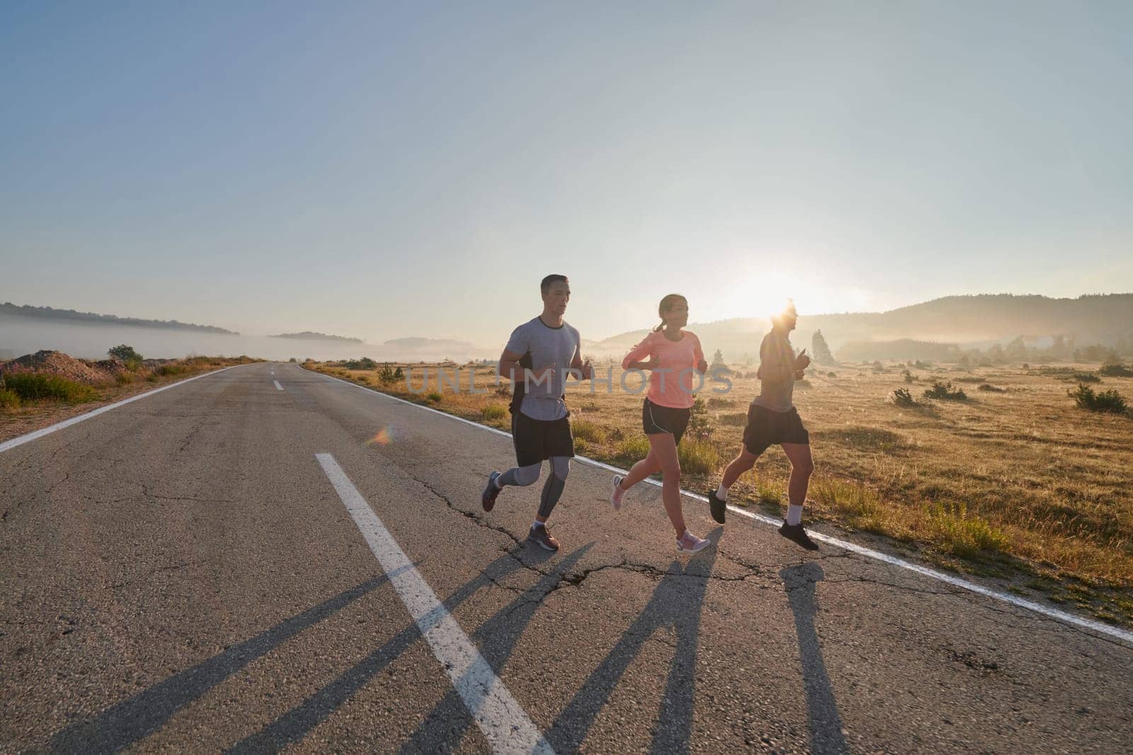 A group of friends, athletes, and joggers embrace the early morning hours as they run through the misty dawn, energized by the rising sun and surrounded by the tranquil beauty of nature.