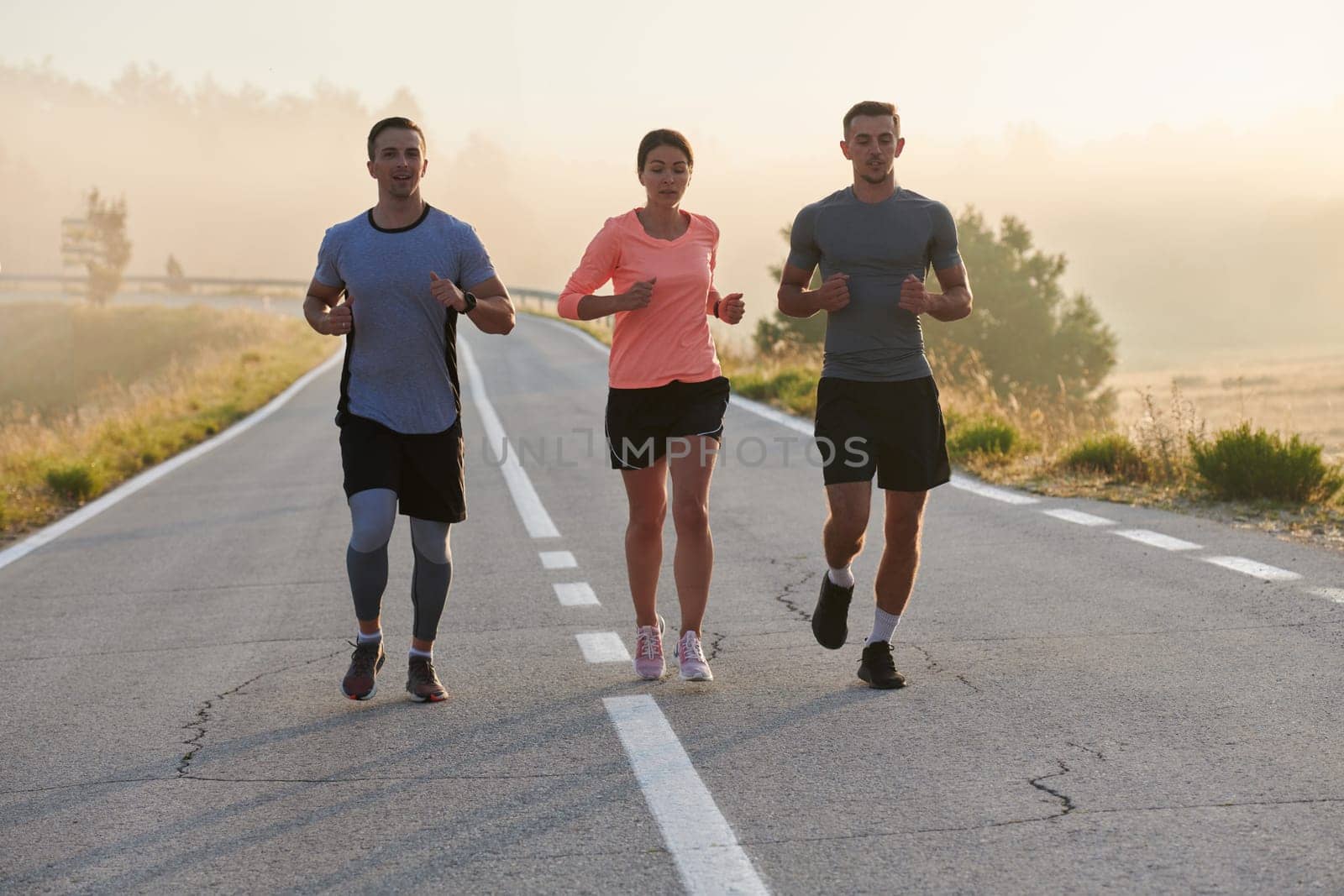 A group of friends, athletes, and joggers embrace the early morning hours as they run through the misty dawn, energized by the rising sun and surrounded by the tranquil beauty of nature.