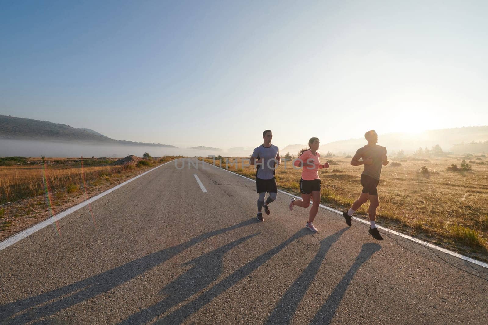 A group of friends, athletes, and joggers embrace the early morning hours as they run through the misty dawn, energized by the rising sun and surrounded by the tranquil beauty of nature.