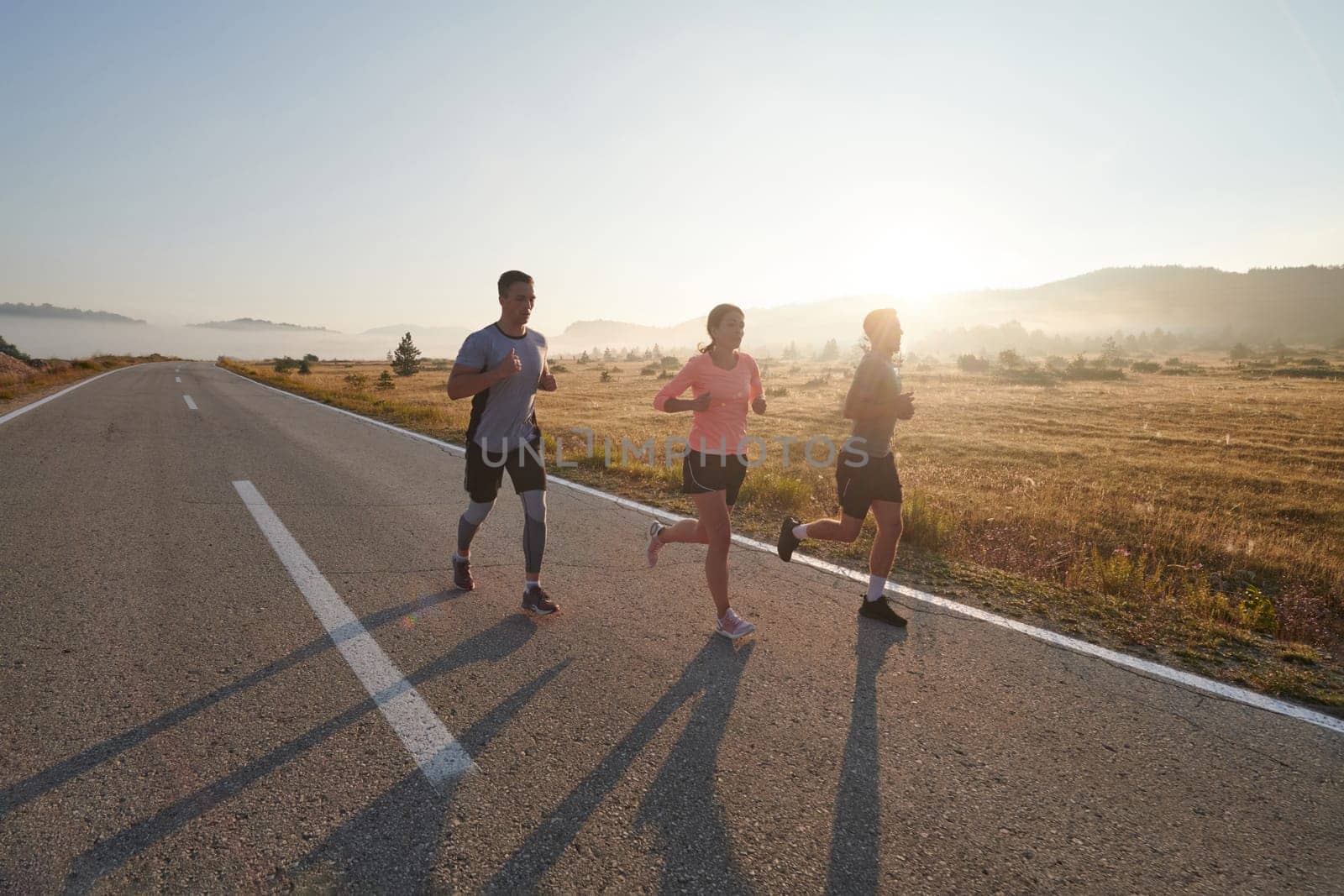 A group of friends, athletes, and joggers embrace the early morning hours as they run through the misty dawn, energized by the rising sun and surrounded by the tranquil beauty of nature by dotshock