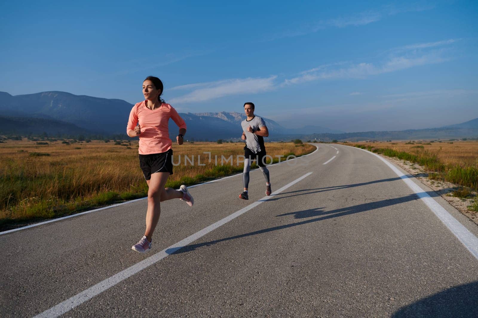 A couple runs through a sun-dappled road, their bodies strong and healthy, their love for each other and the outdoors evident in every stride.