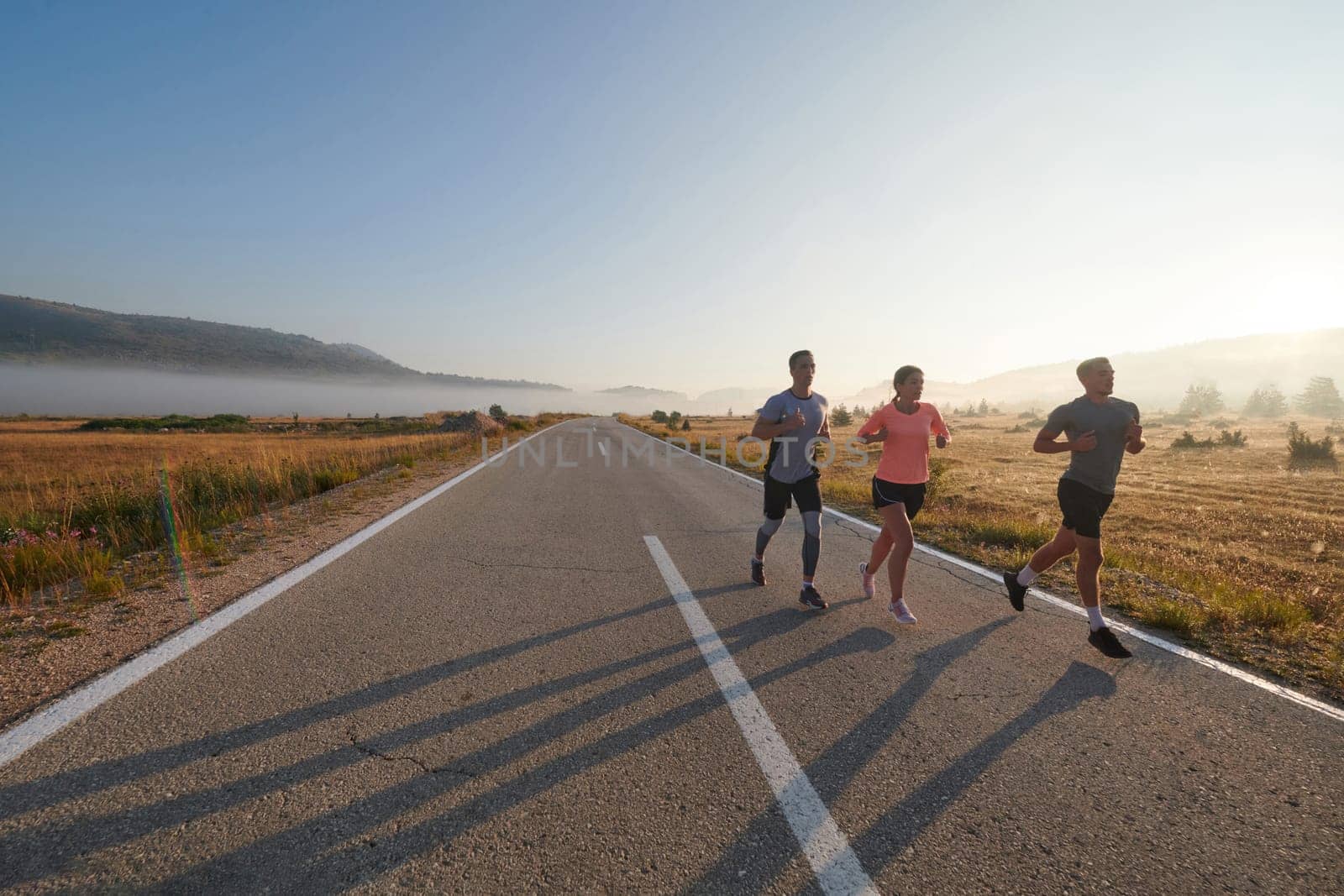 A group of friends, athletes, and joggers embrace the early morning hours as they run through the misty dawn, energized by the rising sun and surrounded by the tranquil beauty of nature.