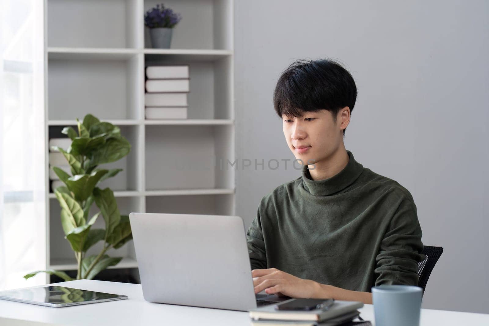 Portrait of a handsome young office worker intently studying how to do a presentation project on a laptop in his office. by wichayada