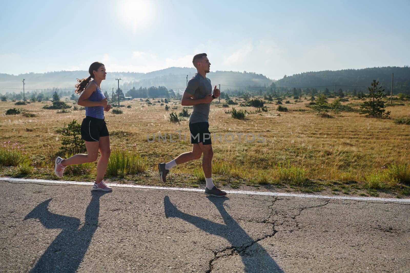 A couple runs through a sun-dappled road, their bodies strong and healthy, their love for each other and the outdoors evident in every stride.