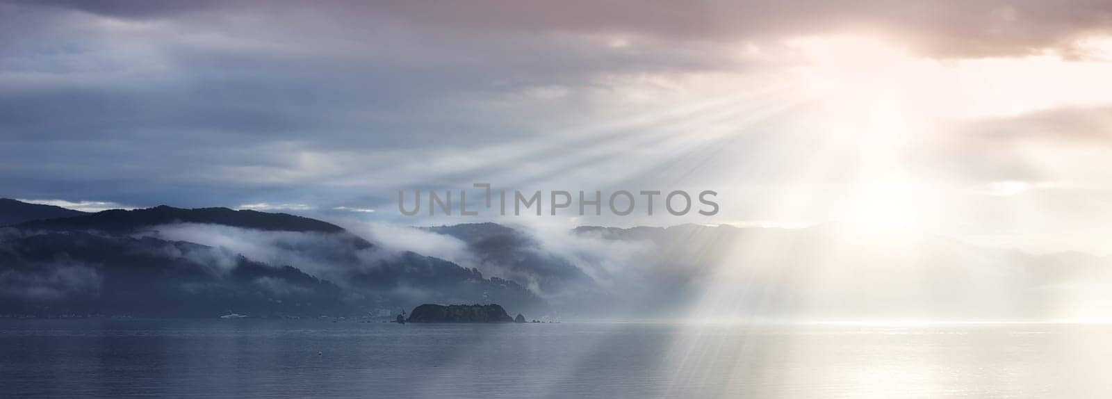 Sun rays, sea and clouds in blue sky with mountains, water and fog in evening. Lake, landscape and environment for holiday in summer, travel and destination for vacation or peace with scenery by YuriArcurs