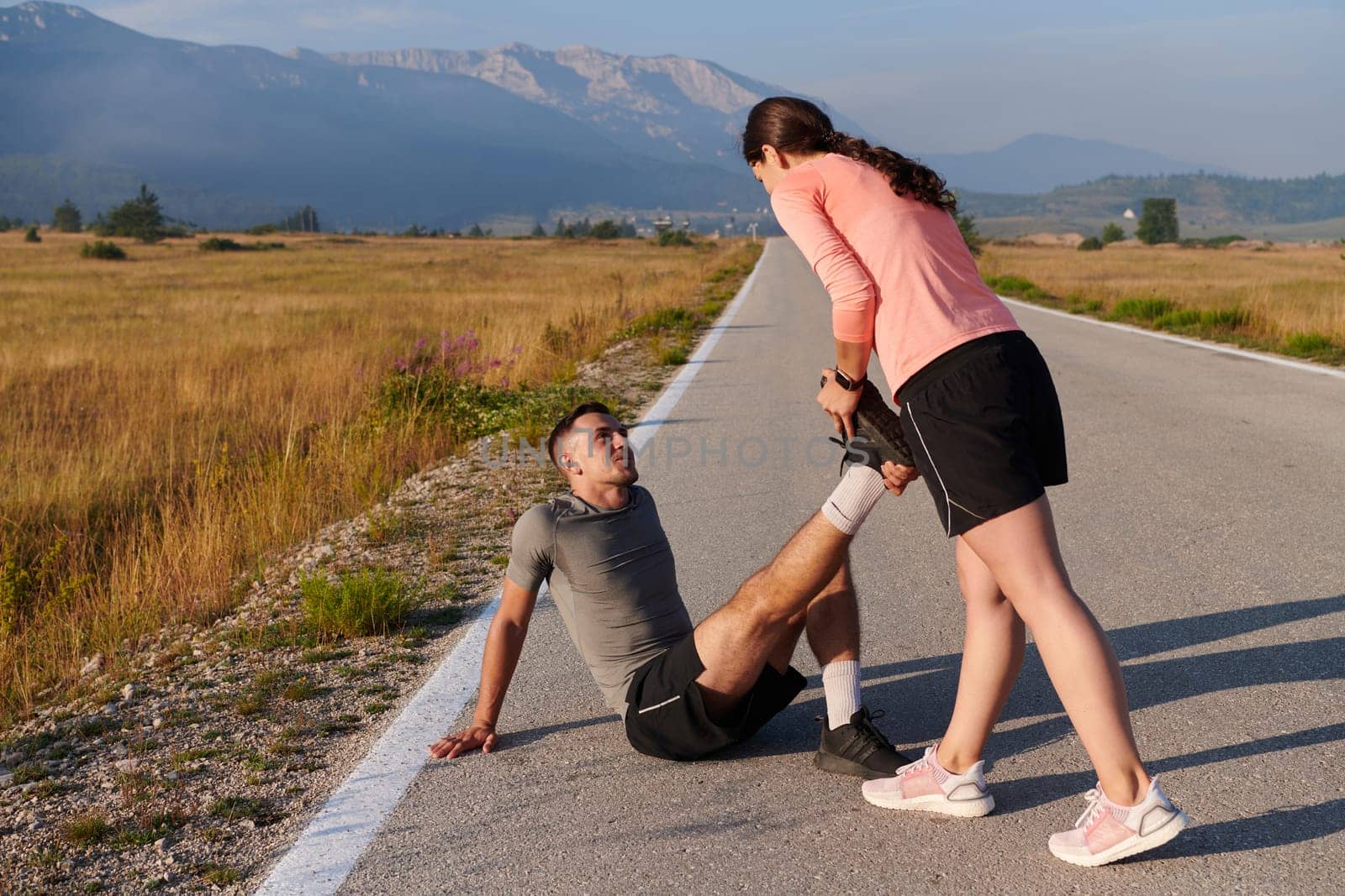 As dawn breaks, a romantic couple engages in a gentle stretch together, symbolizing their shared dedication and preparation for an invigorating early morning run.