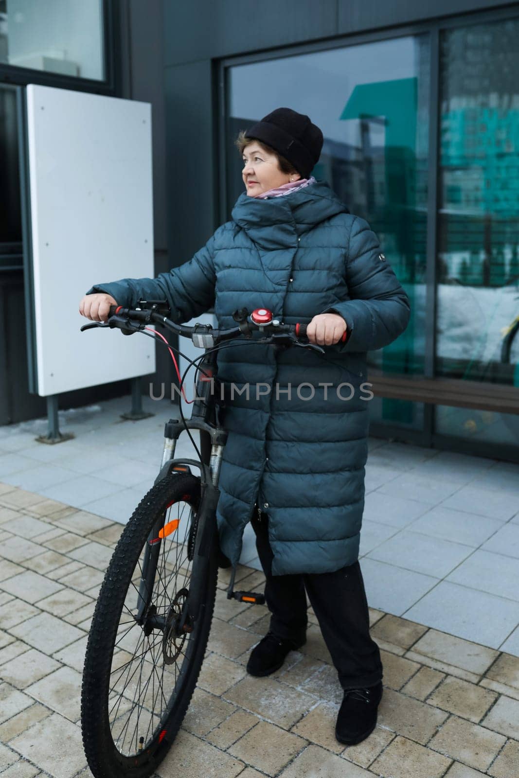 Mature European woman dressed in a winter coat rides a bicycle along the city streets by TRMK