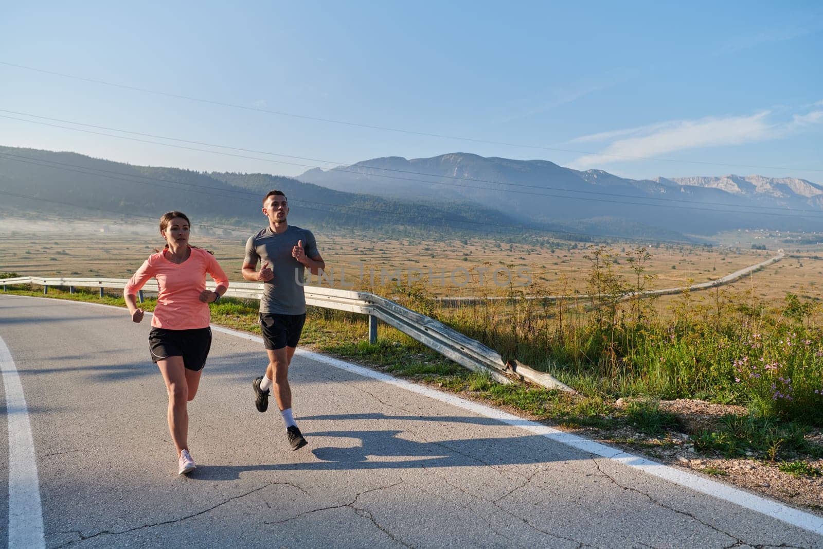 A couple runs through a sun-dappled road, their bodies strong and healthy, their love for each other and the outdoors evident in every stride.