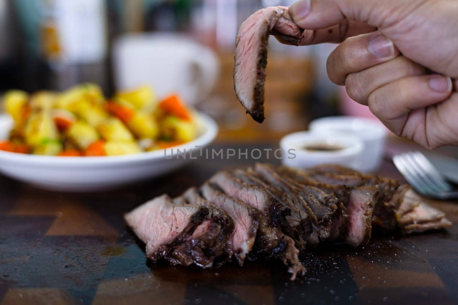 Close-up of female hand holds Pieces of roasted meat. Woman hand holding with grilled beef steak. Concept of eating out.