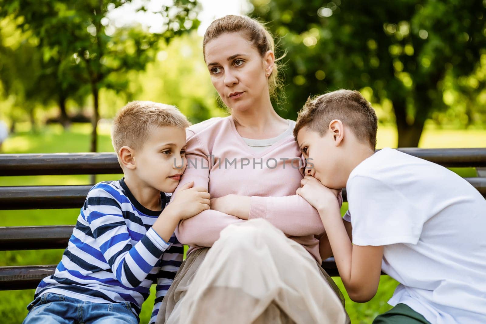 Mother is sitting with her sons on bench in park. She is angry and the boys try to apologize.