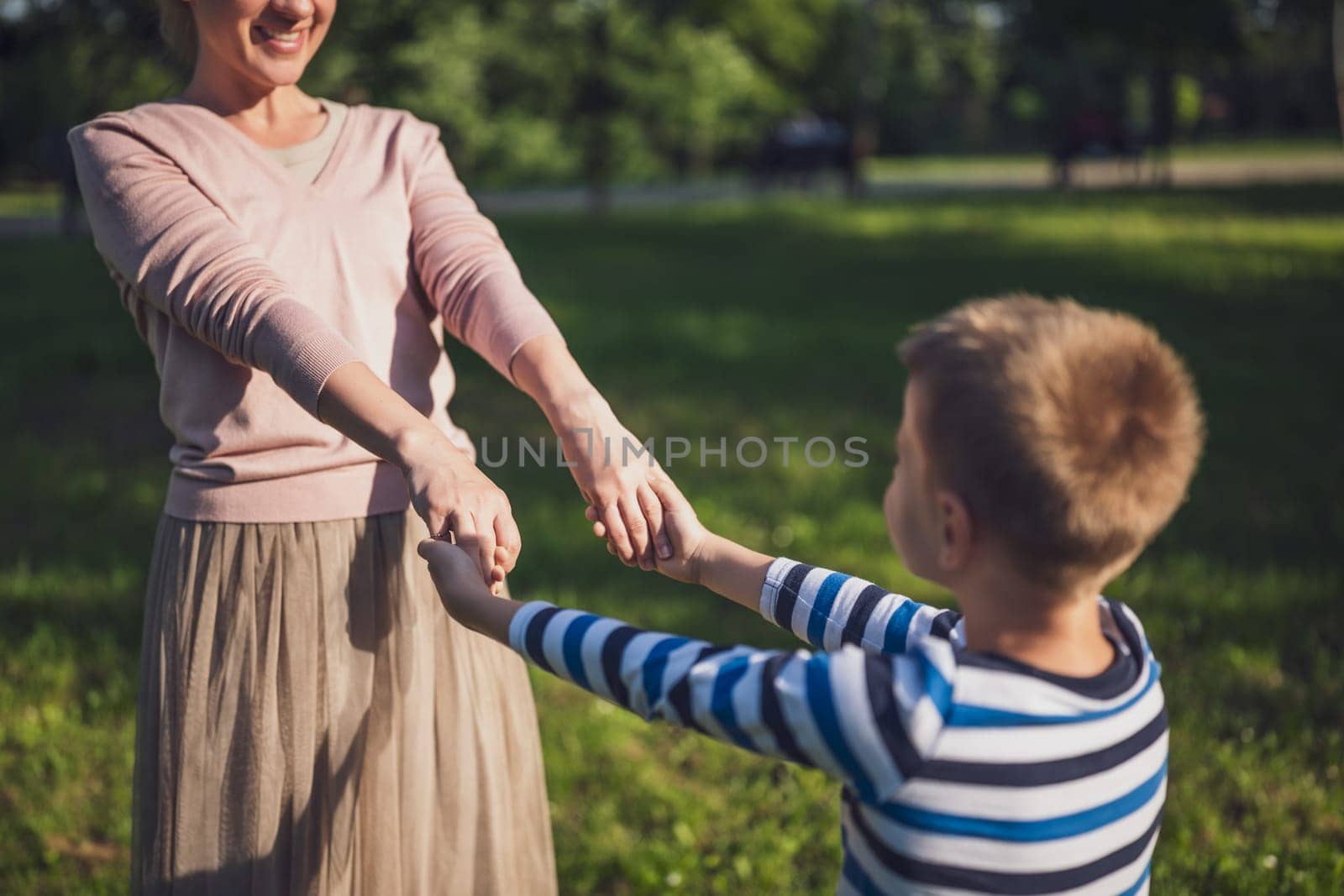 Happy mother is playing with her son in park. They are holding hands.