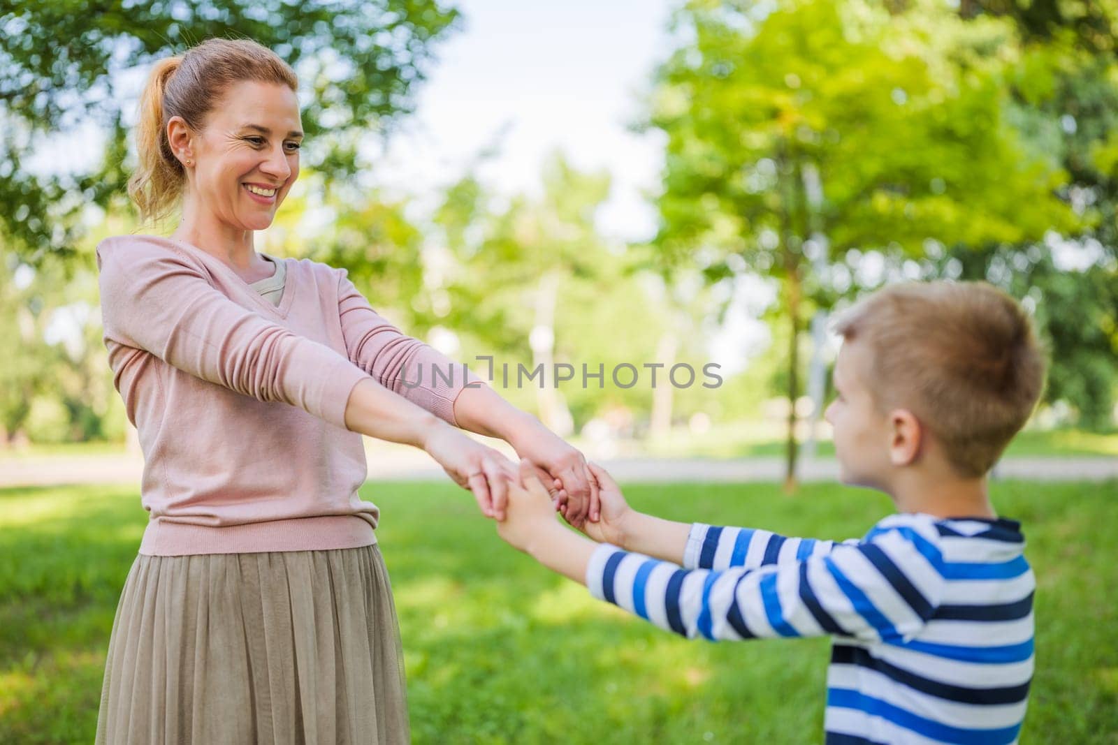 Happy mother is playing with her son in park. They are holding hands.