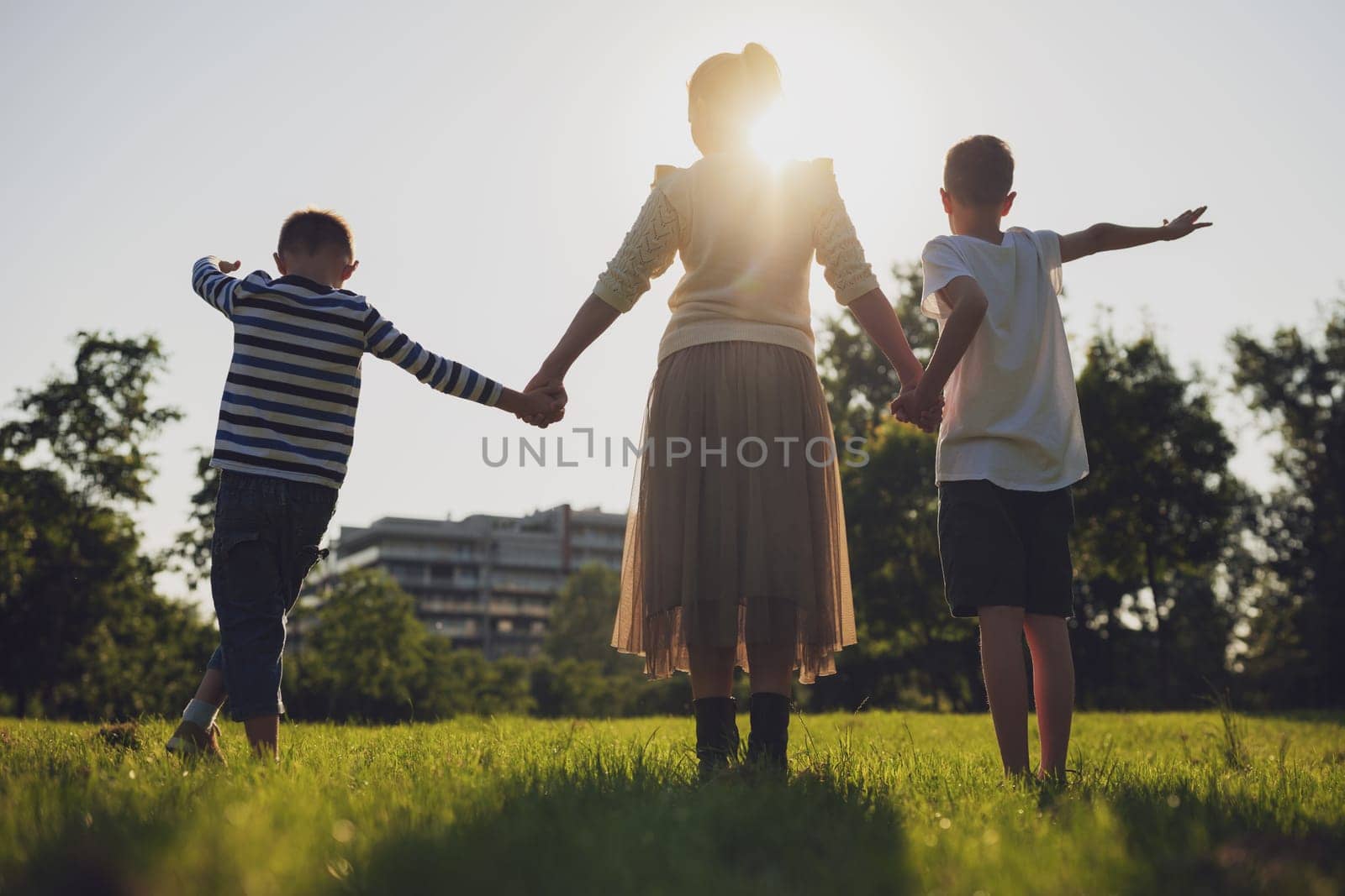 Happy mother is playing with her sons in park. They are holding hands and enjoying sunset.