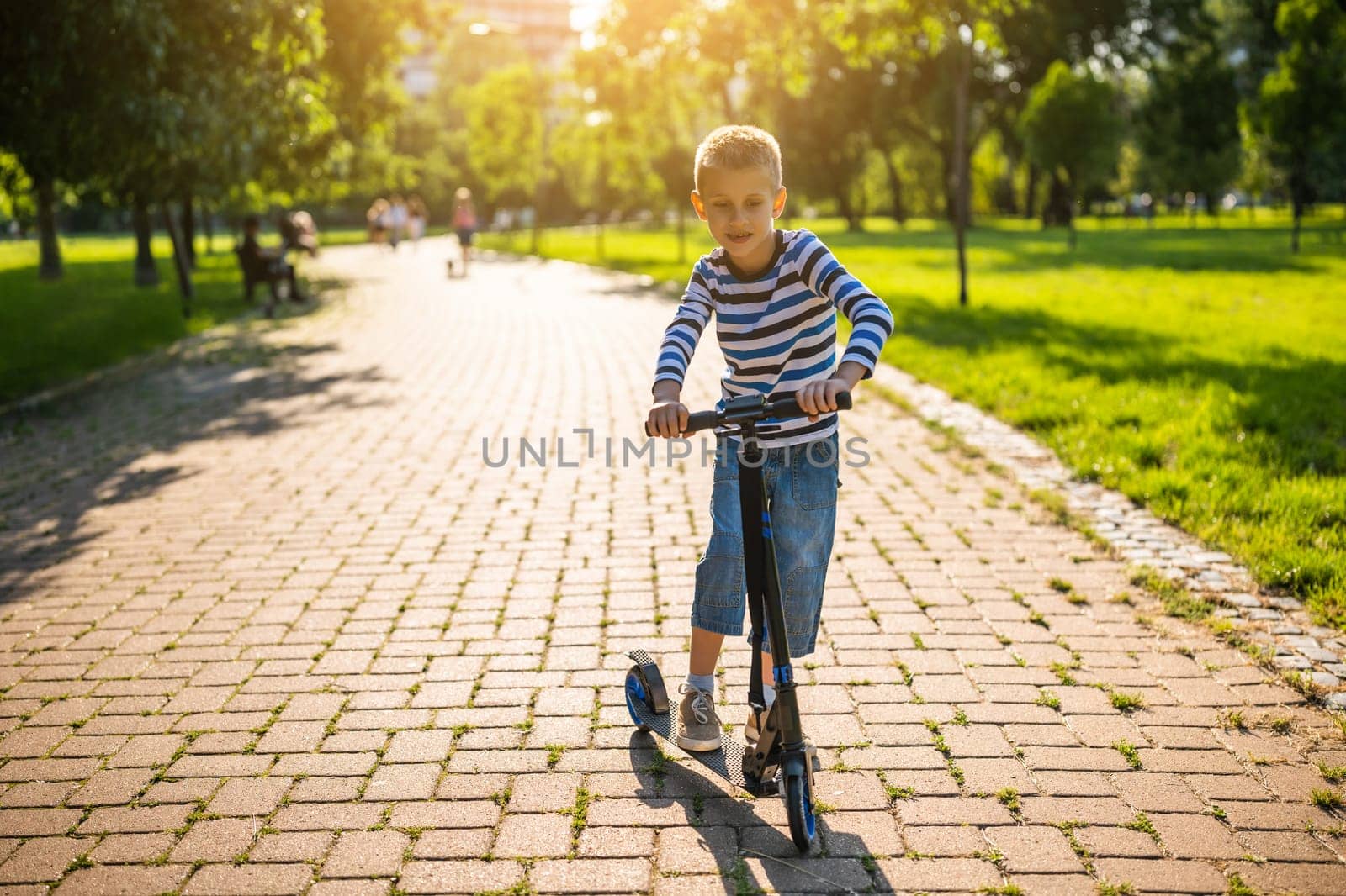 Boy is riding scooter in park on sunny day.