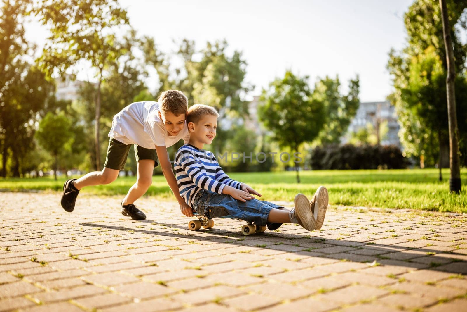 Two boys are having fun with skateboard in park. Playful children in park, happy childhood.
