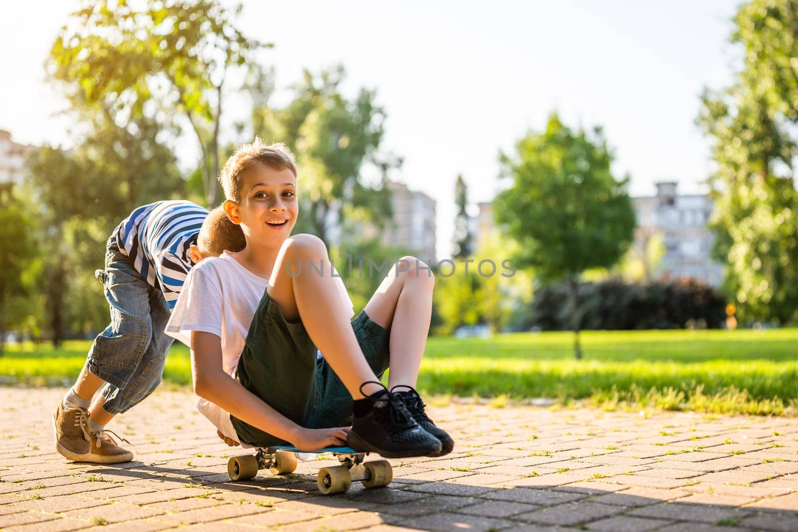 Two boys are having fun with skateboard in park. Playful children in park, happy childhood.