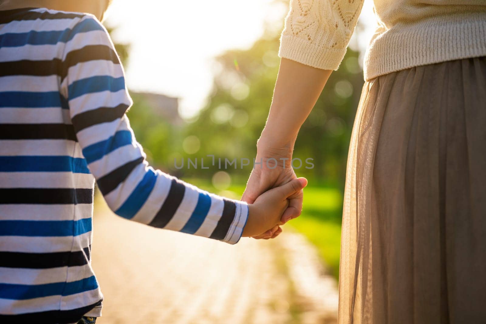 Close up of mother and son holding hands on sunny day.