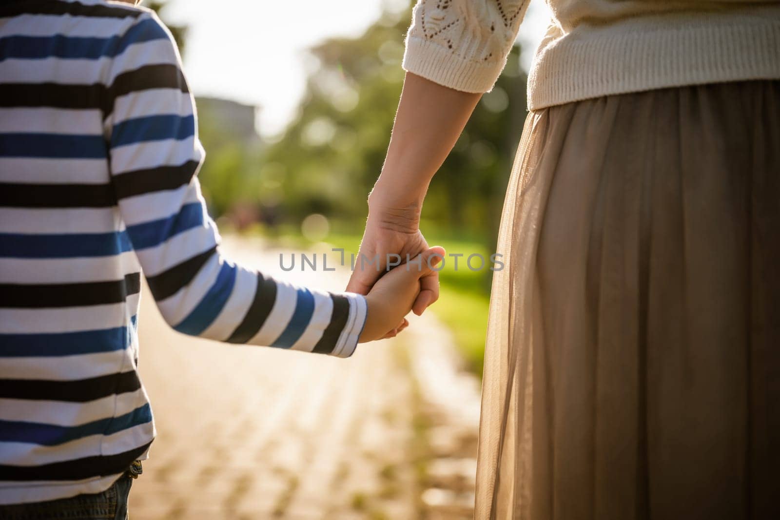 Close up of mother and son holding hands on sunny day.