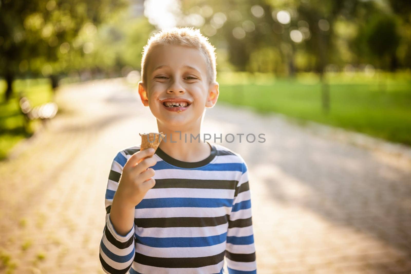 Portrait of happy boy who is standing in park and eating ice cream.