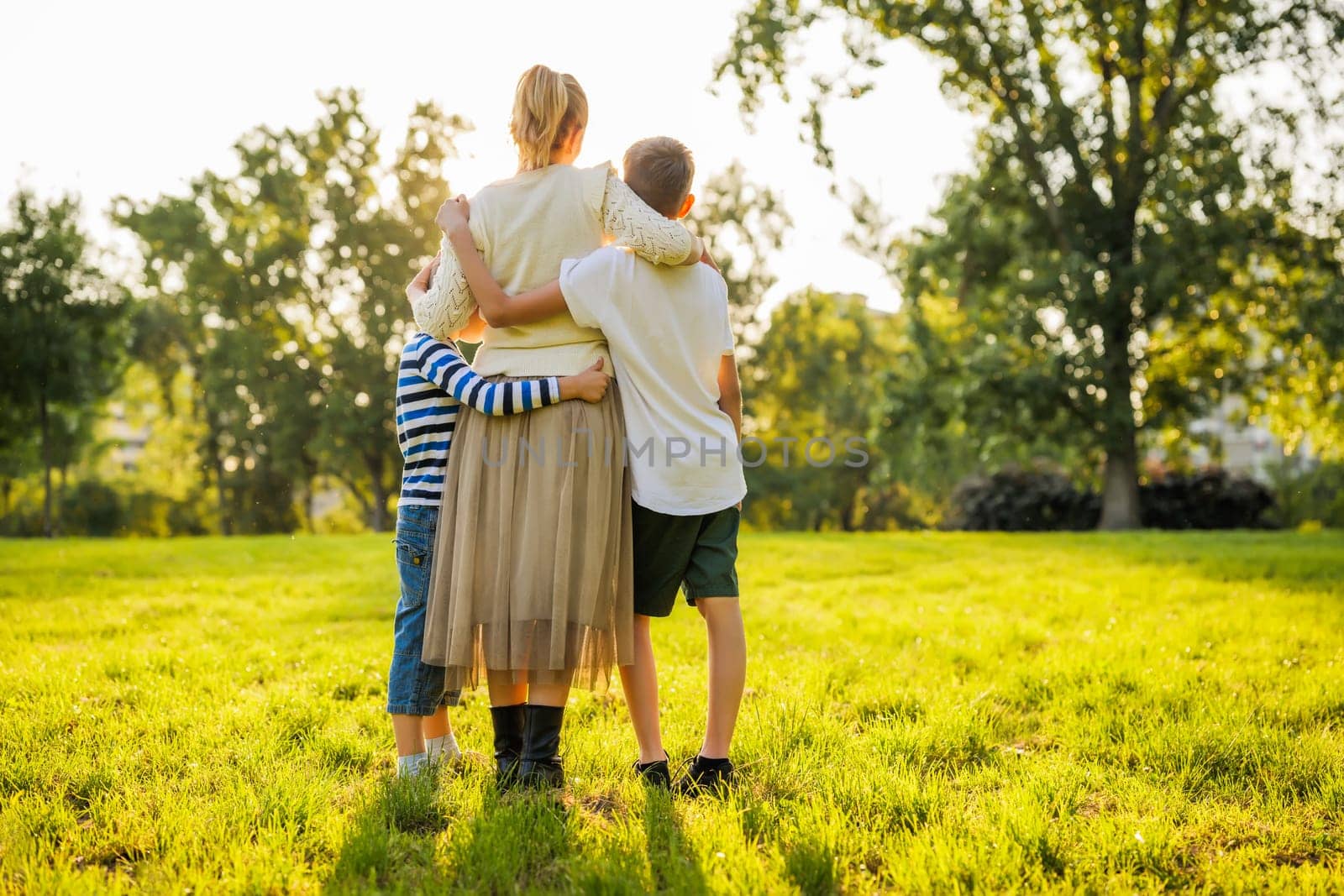 Happy mother is playing with her sons in park. They are holding hands and enjoying sunset.