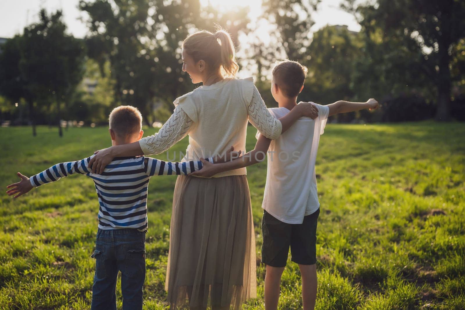 Happy mother is playing with her sons in park. They are holding hands and enjoying sunset.