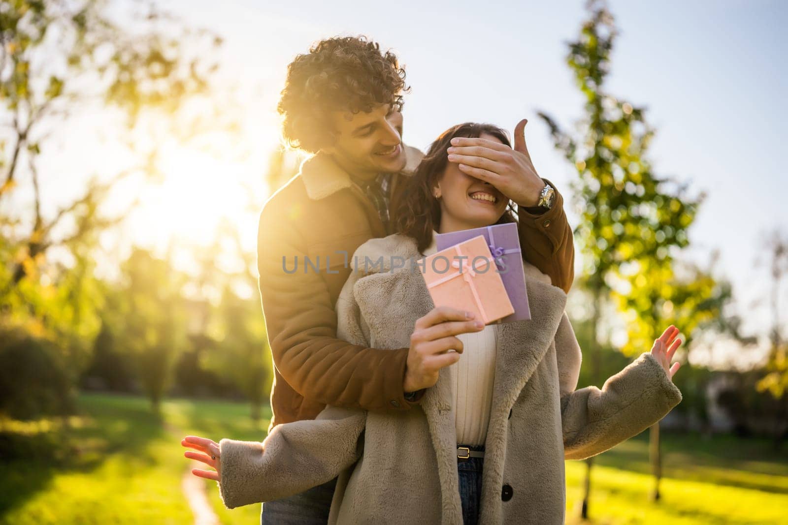 Portrait of happy loving couple in park in sunset. Man is giving present to his woman.