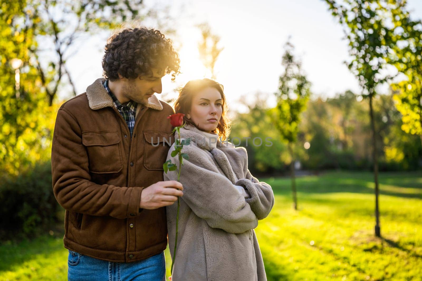 Portrait of happy loving couple in park in sunset. Man is giving rose to his woman.