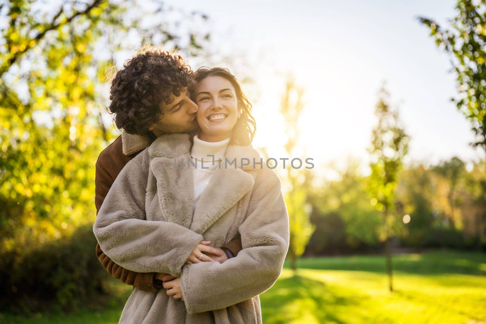 Happy loving couple embracing and kissing in park in sunset.