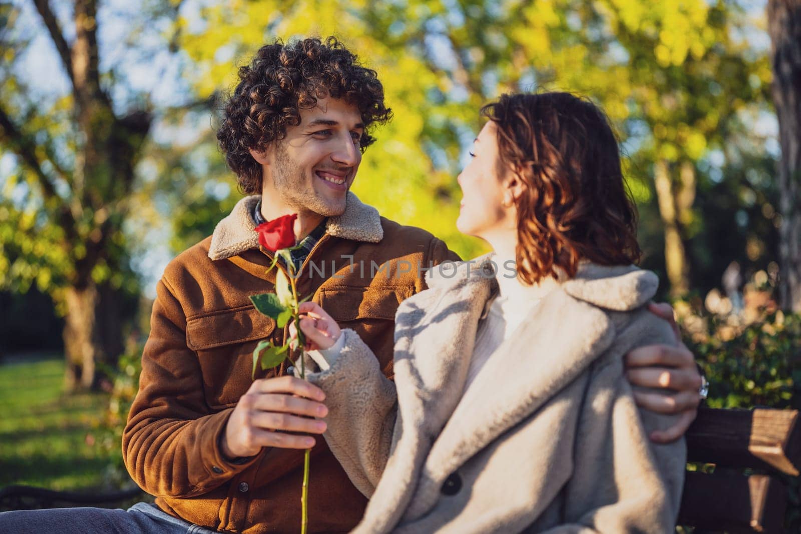 Portrait of happy loving couple in park. Man is giving rose to his woman.