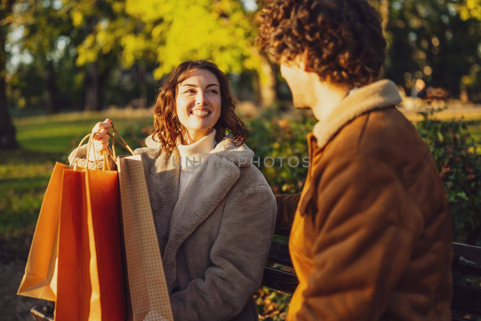 Couple sitting on bench in park. Woman is showing clothes to her man after shopping.