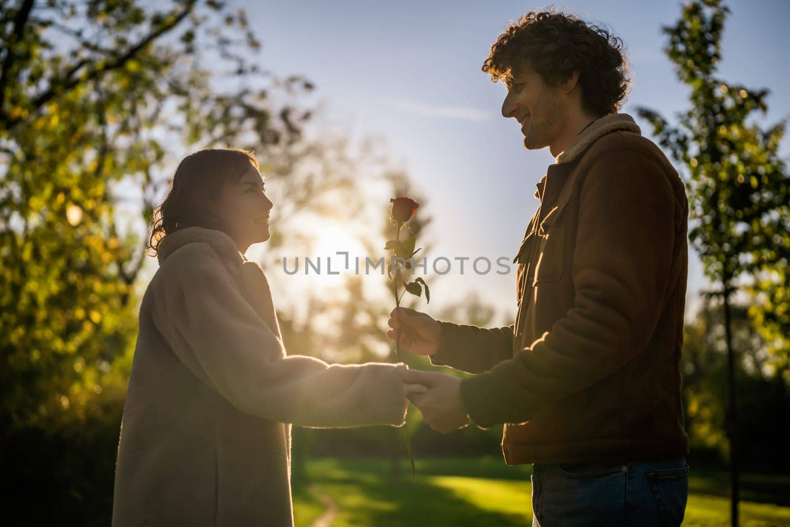Portrait of happy loving couple in park in sunset. Man is giving rose to his woman.