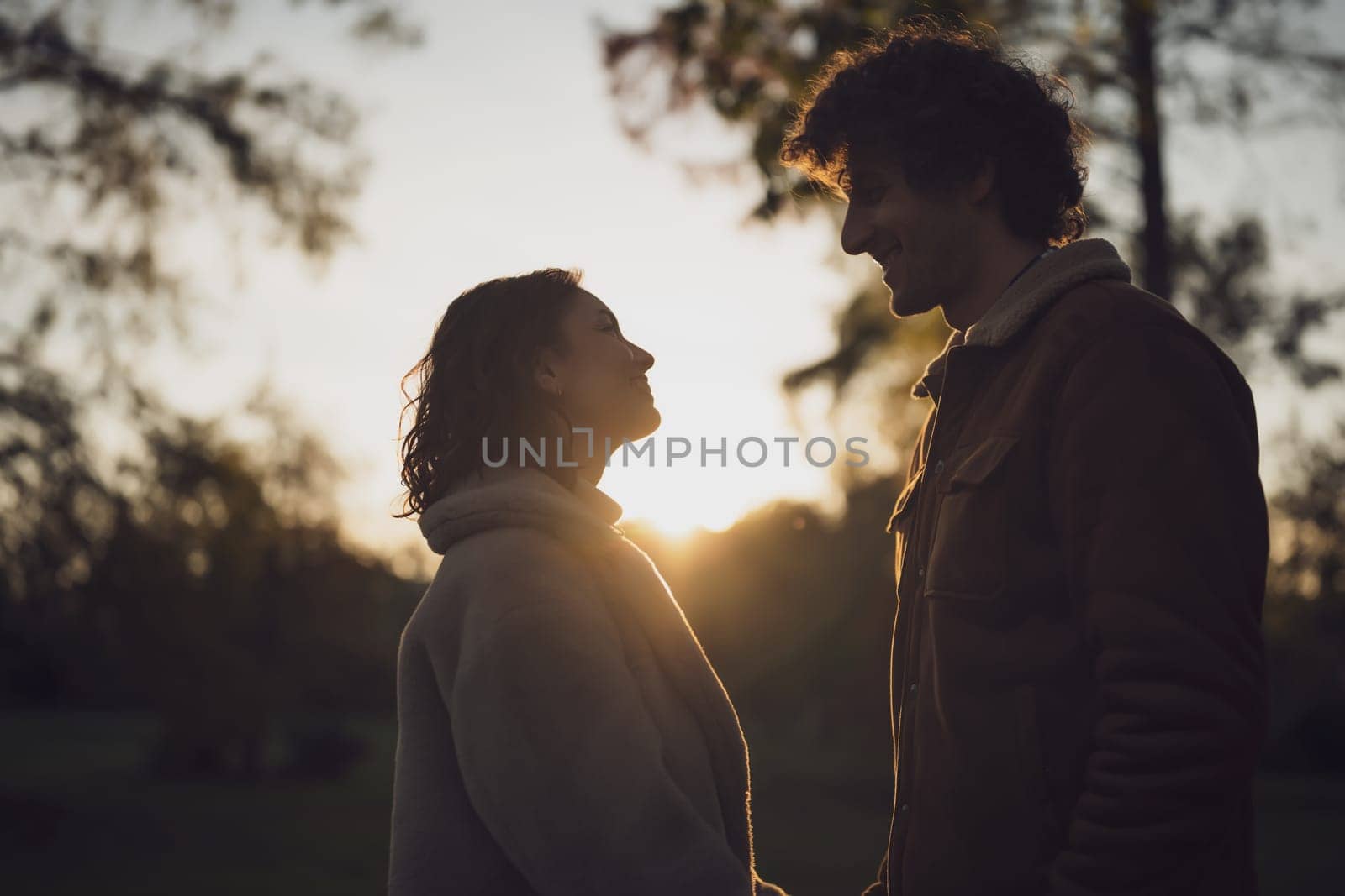 Portrait of happy loving couple in park in sunset. Couple in silhouette looking at each other.