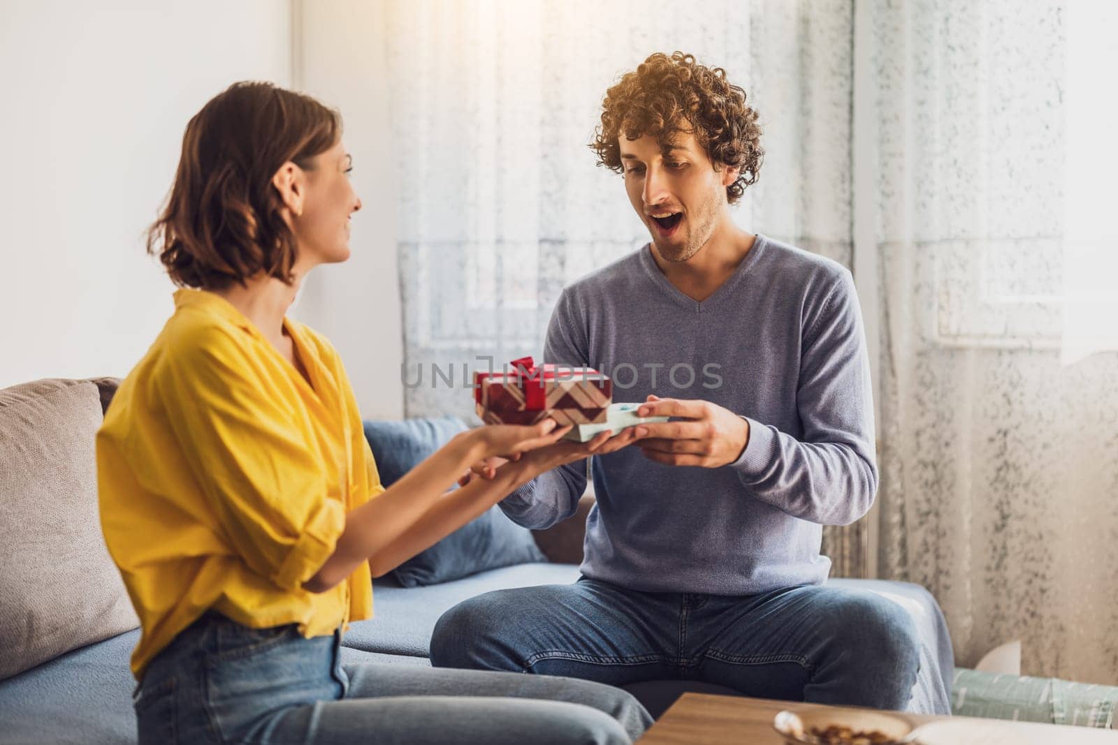 Portrait of young happy couple. Woman is giving gift to her man.