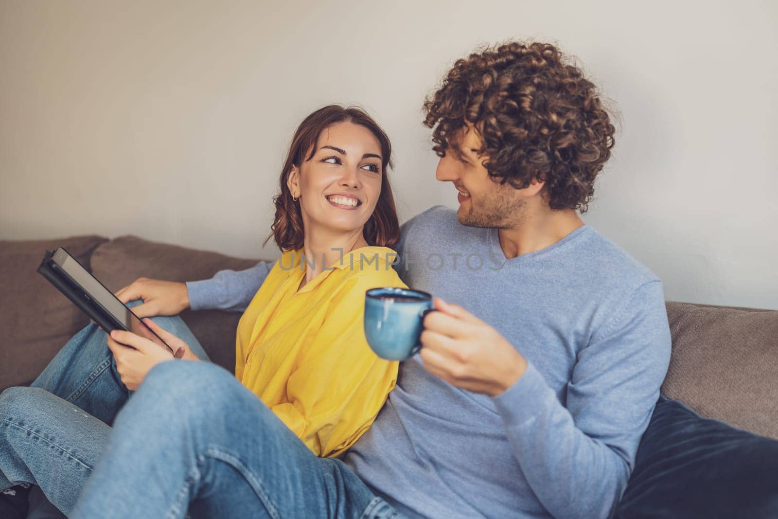 Portrait of young happy couple at home. They are relaxing at sofa.