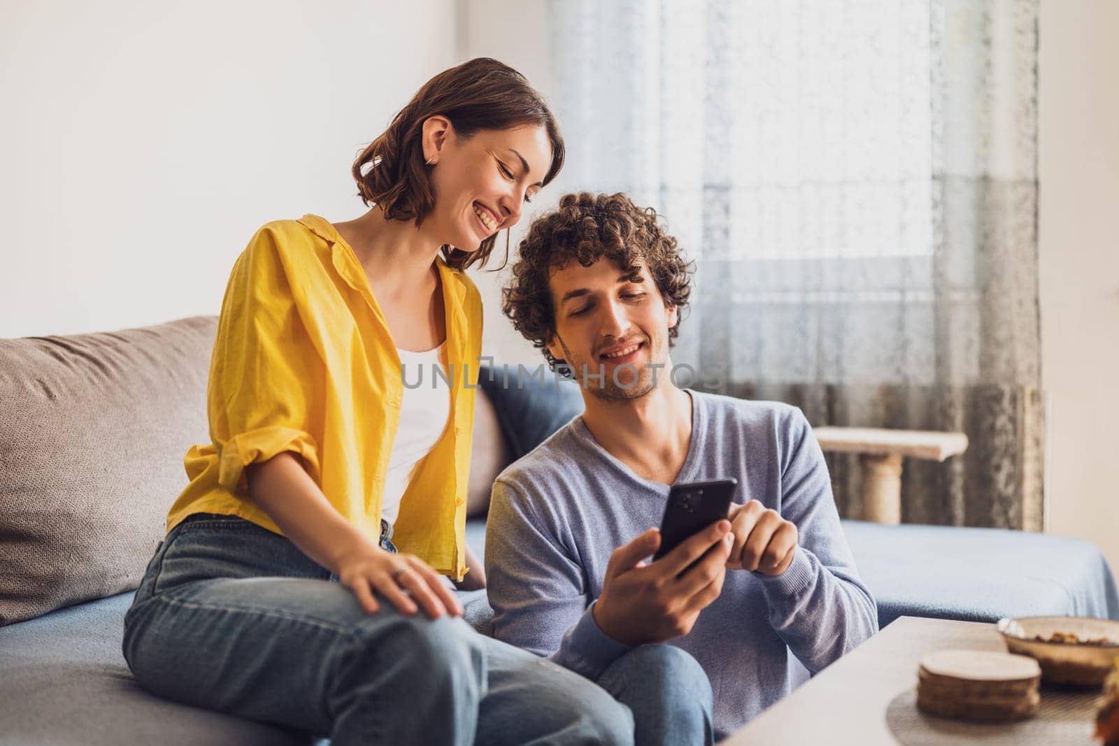 Portrait of young happy couple who is looking at smartphone at home.