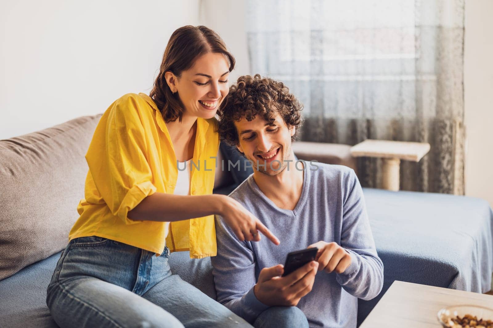 Portrait of young happy couple who is looking at smartphone at home.