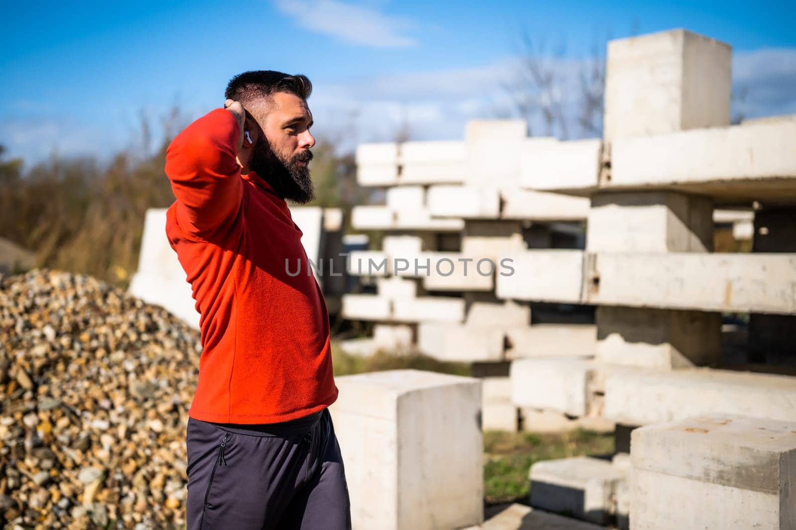 Adult man is exercising outdoor on sunny day. He is stretching his body.