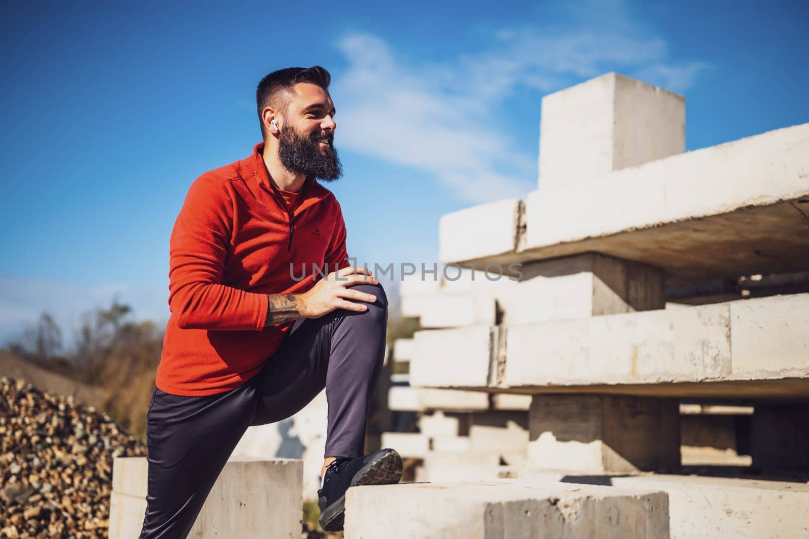 Adult man is exercising outdoor on sunny day. He is stretching his body.