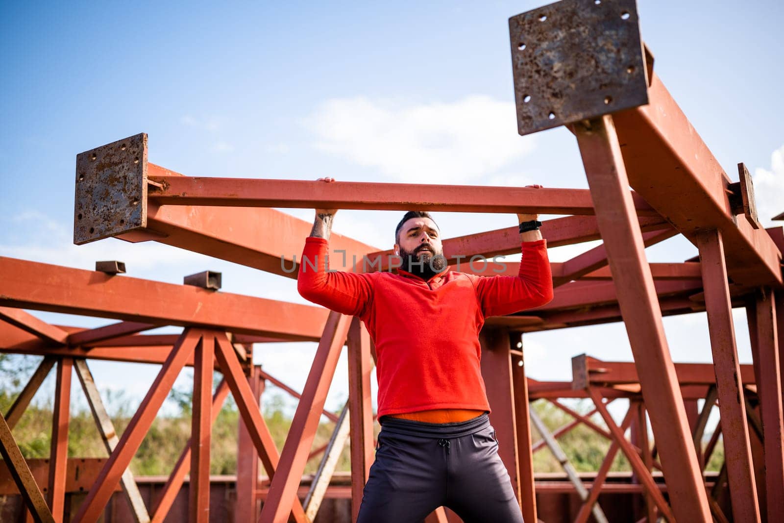 Young man is exercising outdoor. He is doing pull-ups.