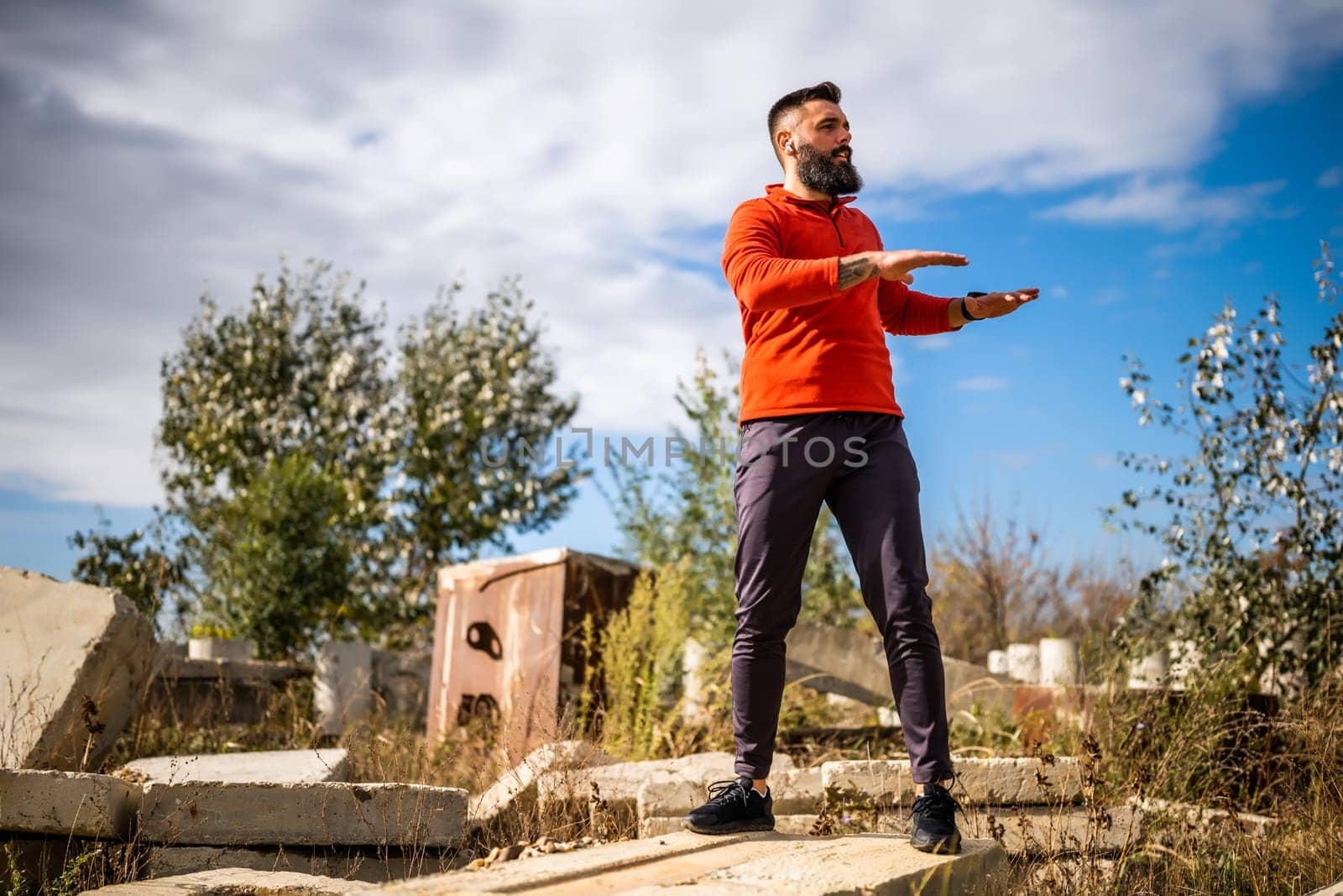 Adult man is exercising outdoor on sunny day. He is stretching his body.